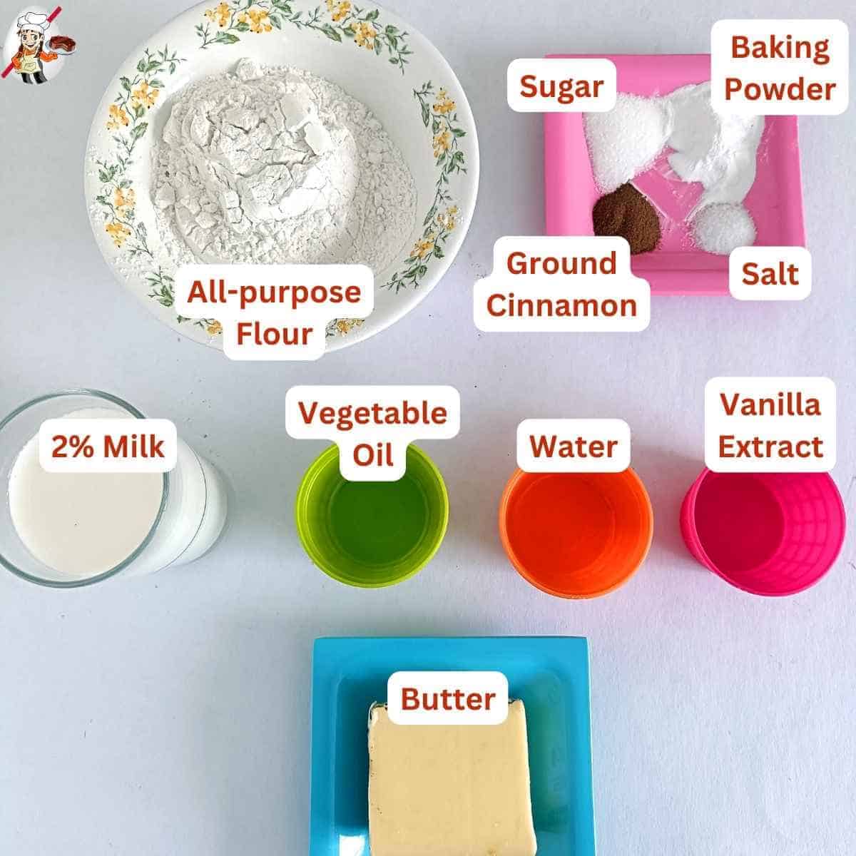 The ingredients include all-purpose flour in a floral-patterned bowl, sugar, baking powder, ground cinnamon, and salt on a pink plate, 2% milk in a glass, vegetable oil in a green cup, water in an orange cup, vanilla extract in a pink cup, and butter on a blue plate. 